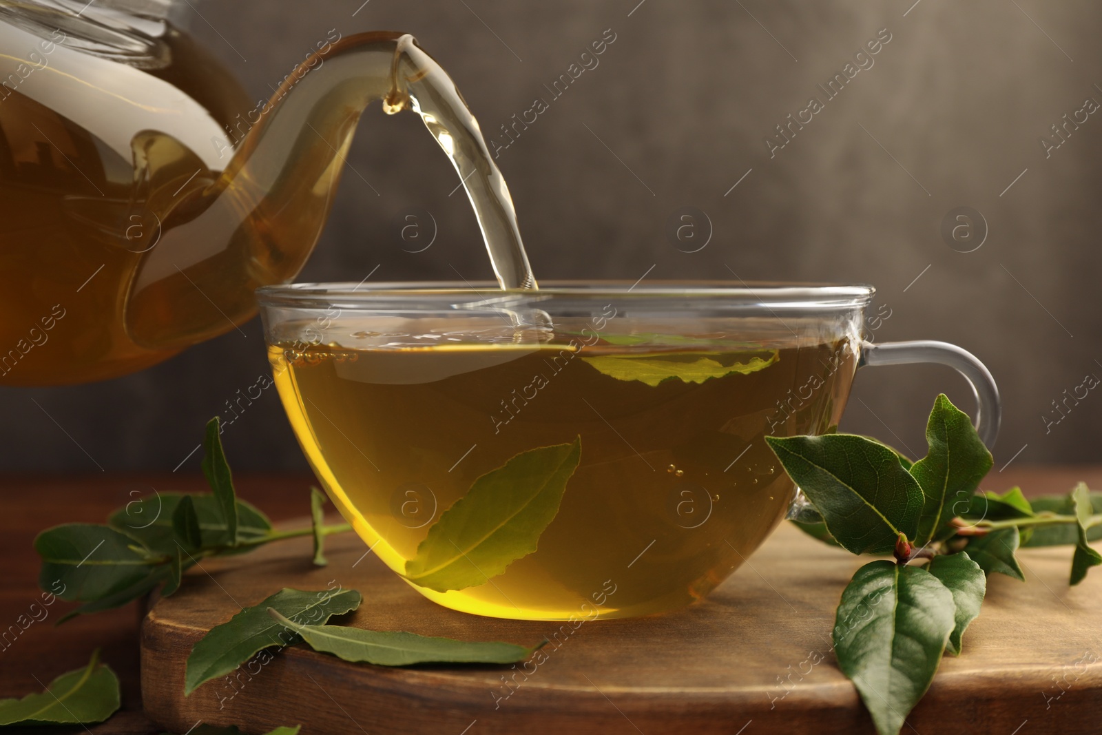 Photo of Pouring freshly brewed tea with bay leaves into cup on wooden board, closeup