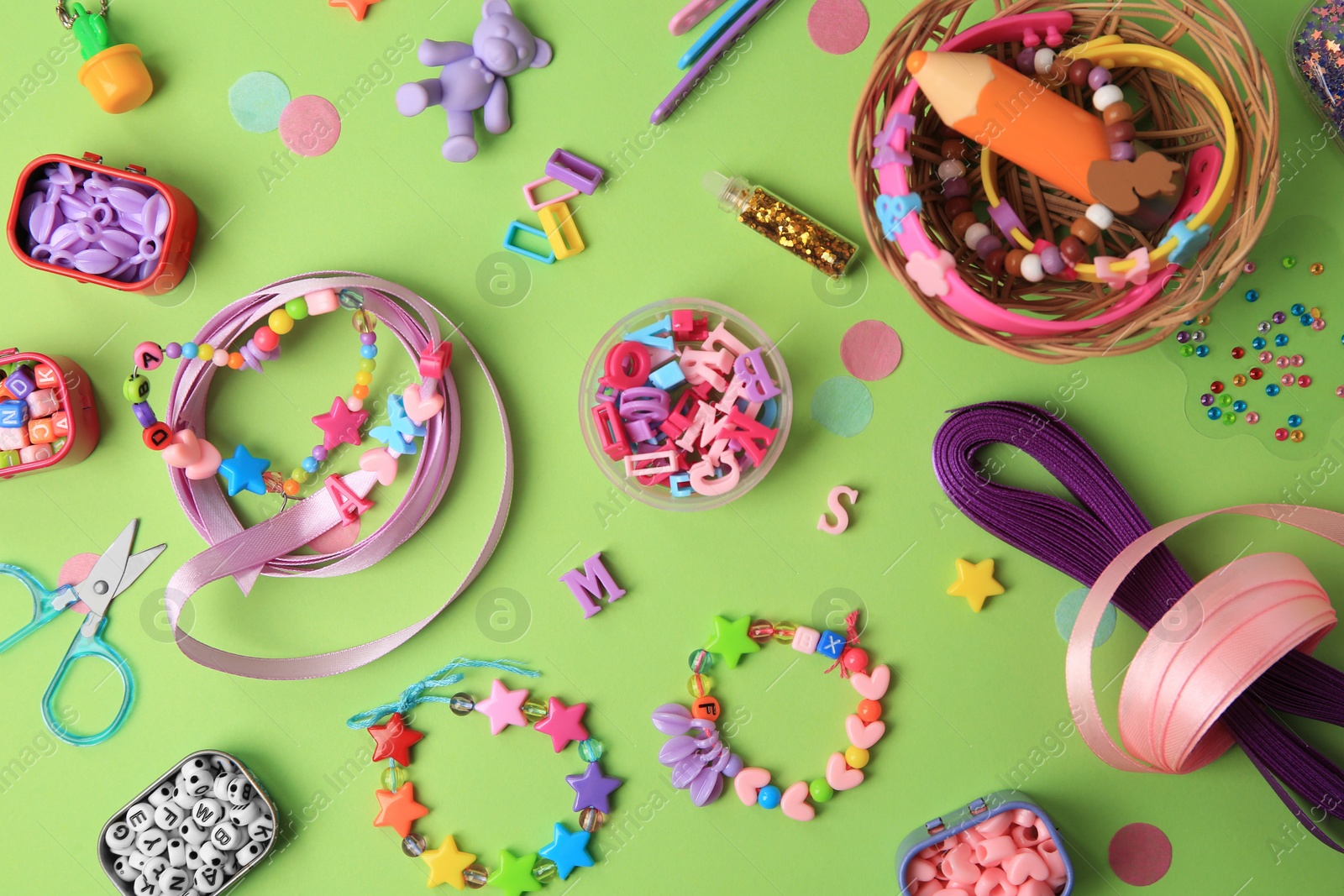 Photo of Handmade jewelry kit for children. Colorful beads, ribbons and supplies on green background, flat lay