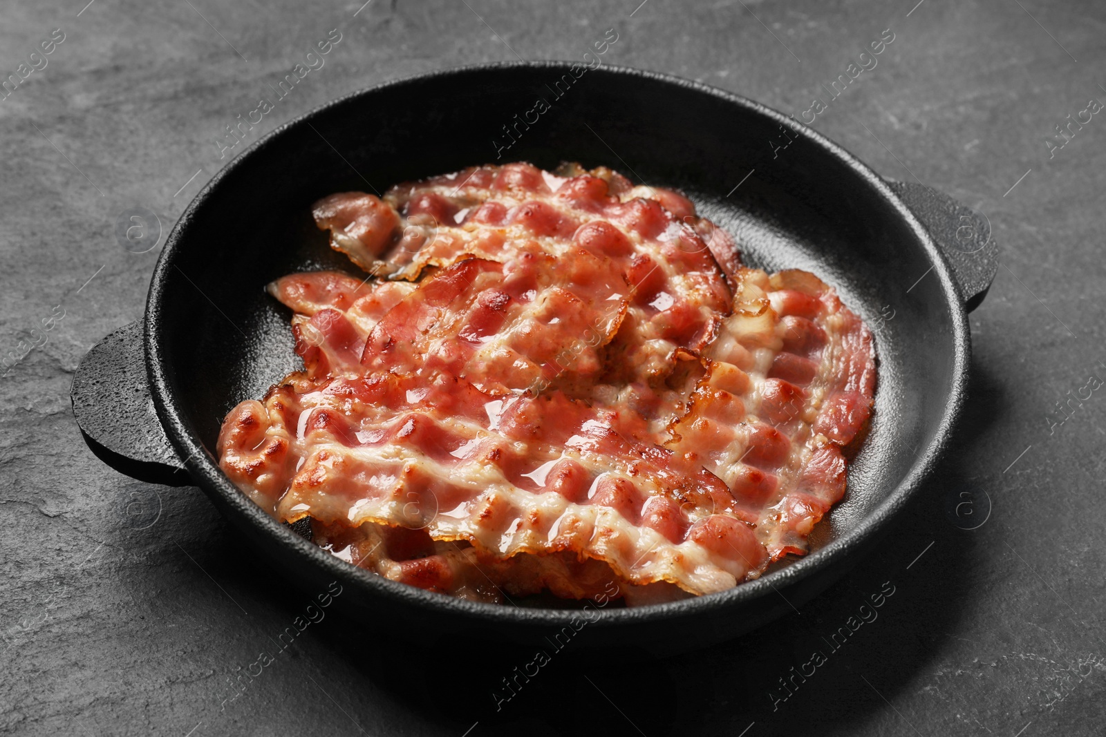 Photo of Fried bacon slices on dark textured table, closeup