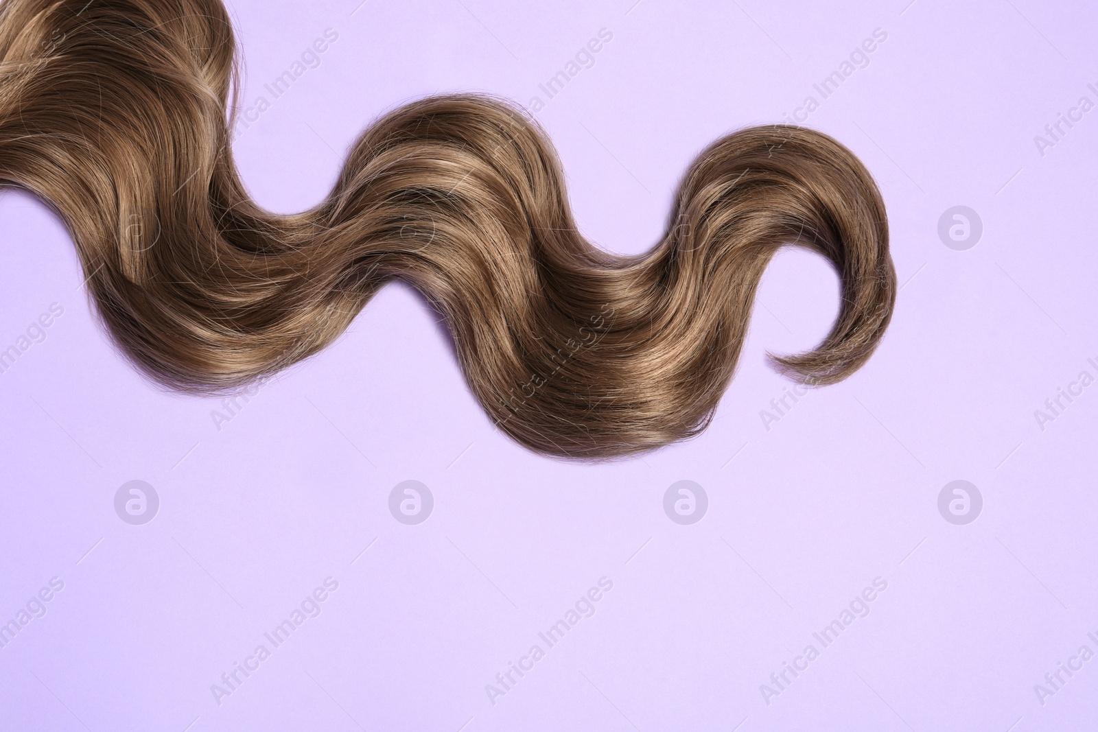 Photo of Lock of brown wavy hair on color background, top view. Space for text