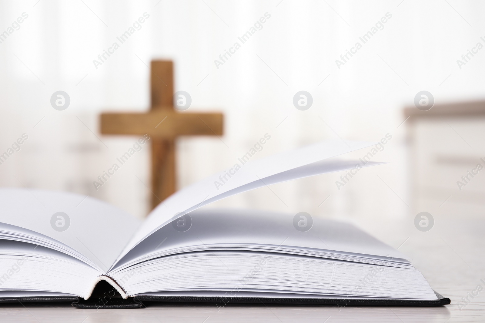 Photo of Open Bible on table and blurred cross on background, closeup. Christian religion