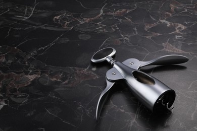 Photo of One wing corkscrew on black marble table. Space for text