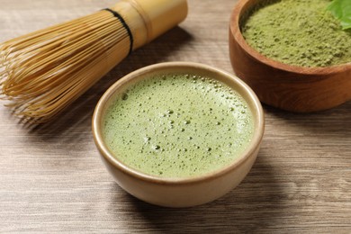 Cup of fresh matcha tea, bamboo whisk and green powder on wooden table, closeup