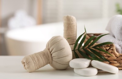 Spa composition. Herbal bags, stones and palm leaves on white table indoors, closeup