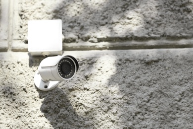 Photo of Modern CCTV security camera on stone building wall outdoors. Space for text