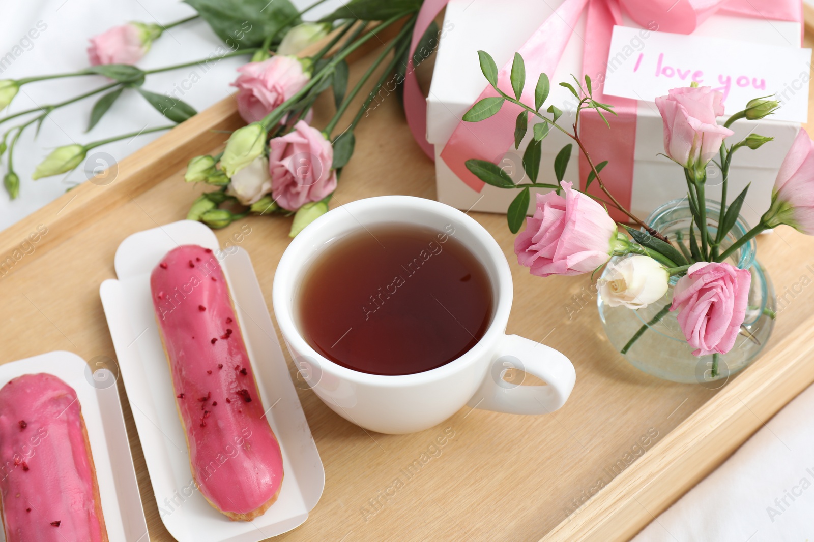 Photo of Tasty breakfast served in bed. Delicious eclairs, tea, gift box, flowers and card with phrase I Love You on tray