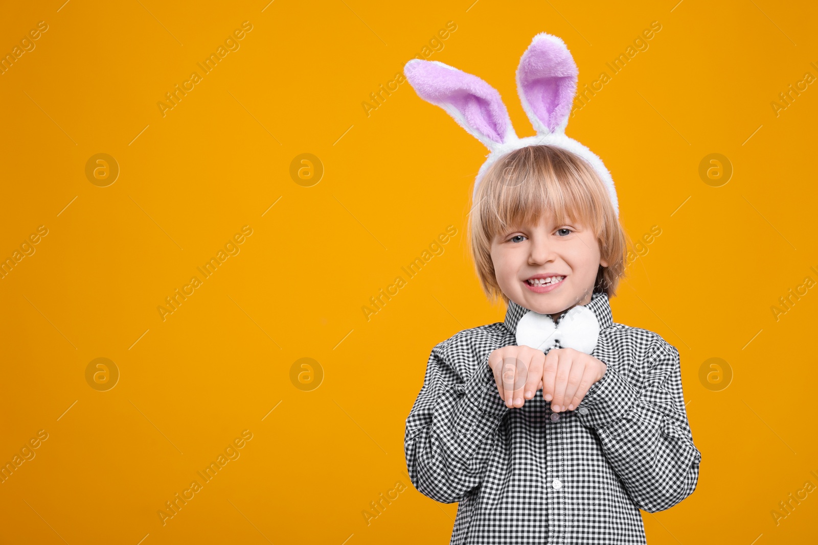 Photo of Happy boy wearing bunny ears headband on orange background, space for text. Easter celebration