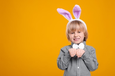 Happy boy wearing bunny ears headband on orange background, space for text. Easter celebration