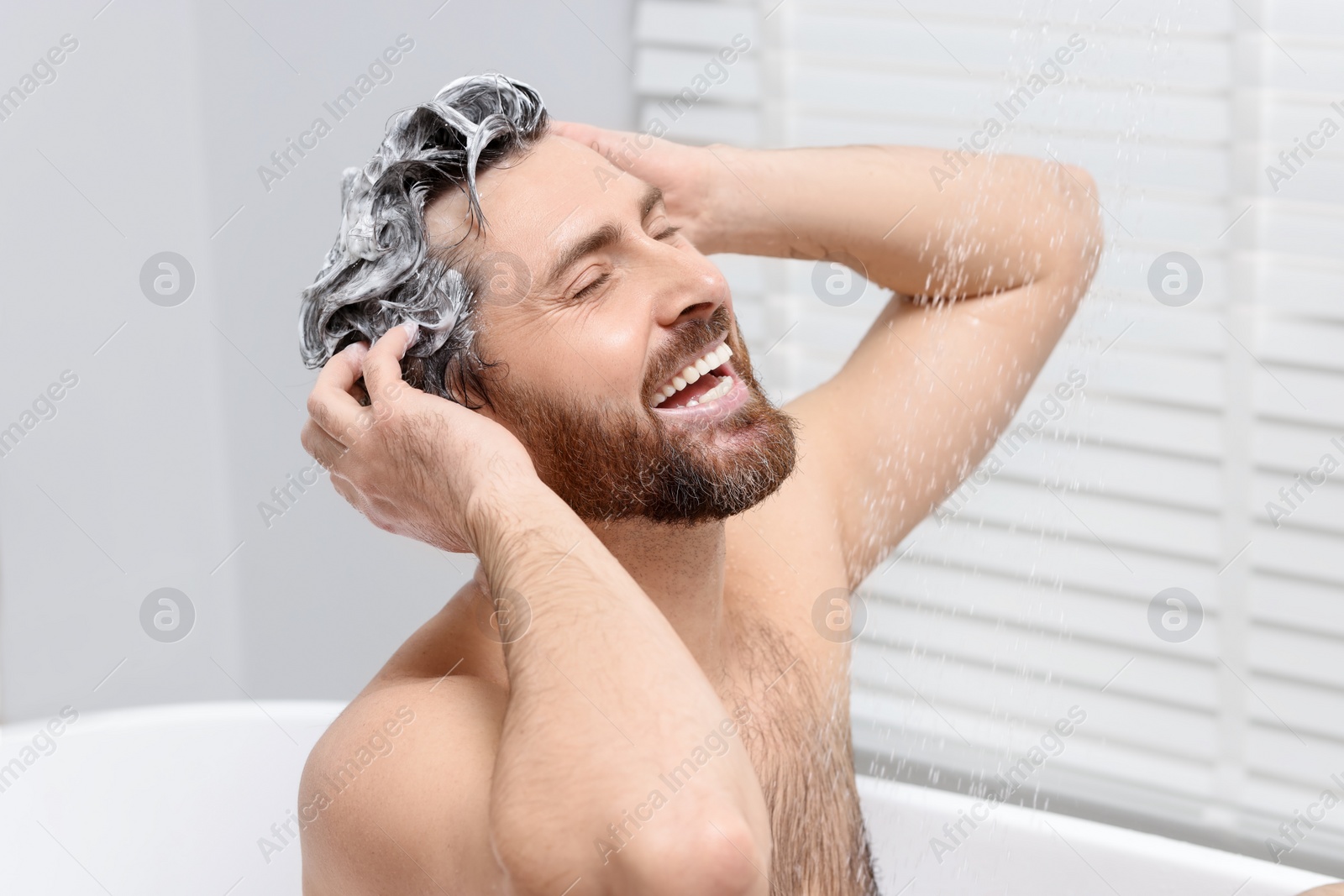 Photo of Happy man washing his hair with shampoo in shower