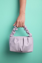 Photo of Woman holding stylish bag on turquoise background, closeup