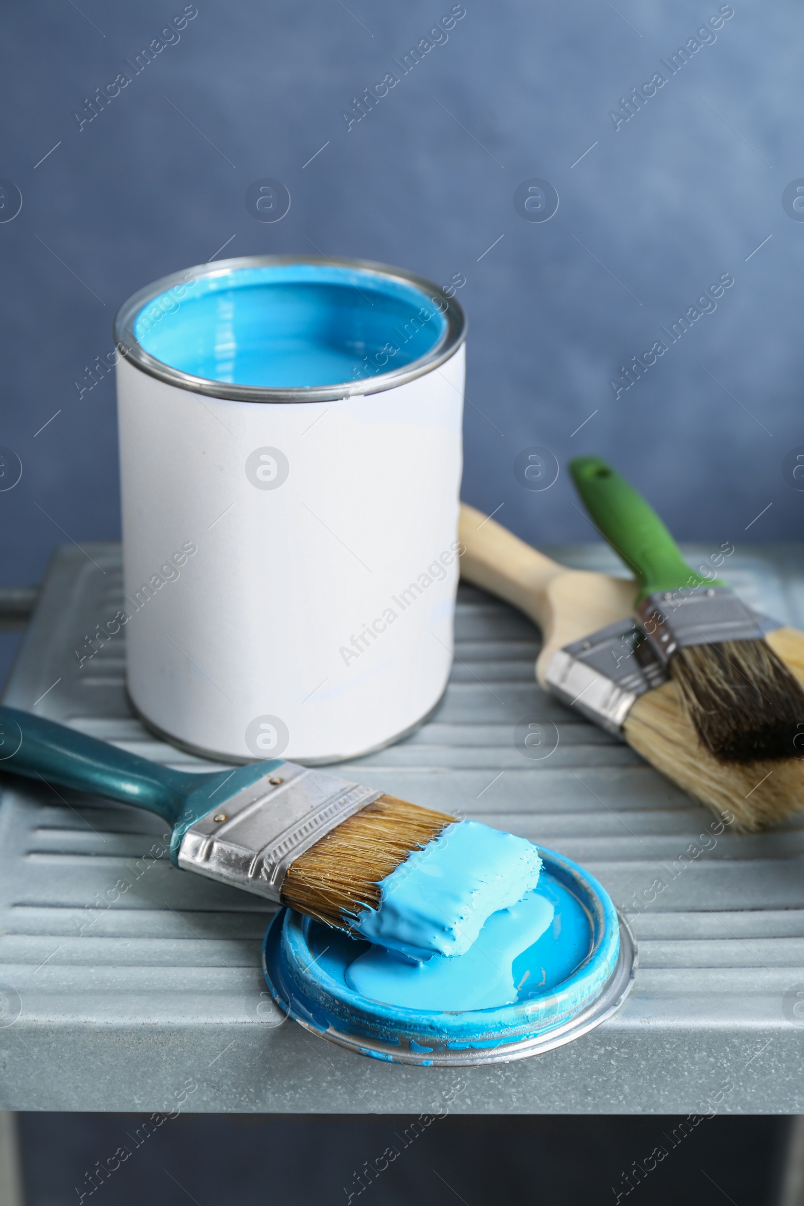 Photo of Can of light blue paint and brushes on metal ladder