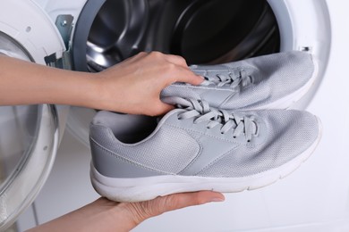 Woman putting pair of sport shoes into washing machine, closeup