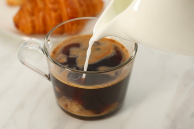 Photo of Pouring milk in coffee at white table, closeup