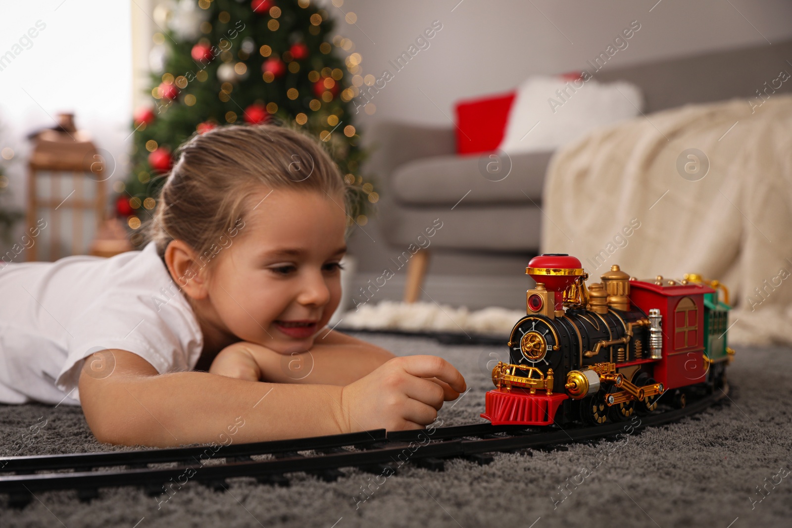 Photo of Little girl playing with colorful train toy in room decorated for Christmas