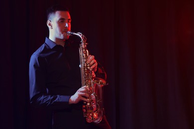 Photo of Young man playing saxophone on dark background. Space for text
