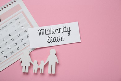 Photo of Card with phrase Maternity Leave, calendar and figures of family on pink background, flat lay. Space for text