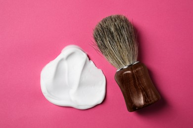 Photo of Brush and sample of shaving foam on pink background, flat lay
