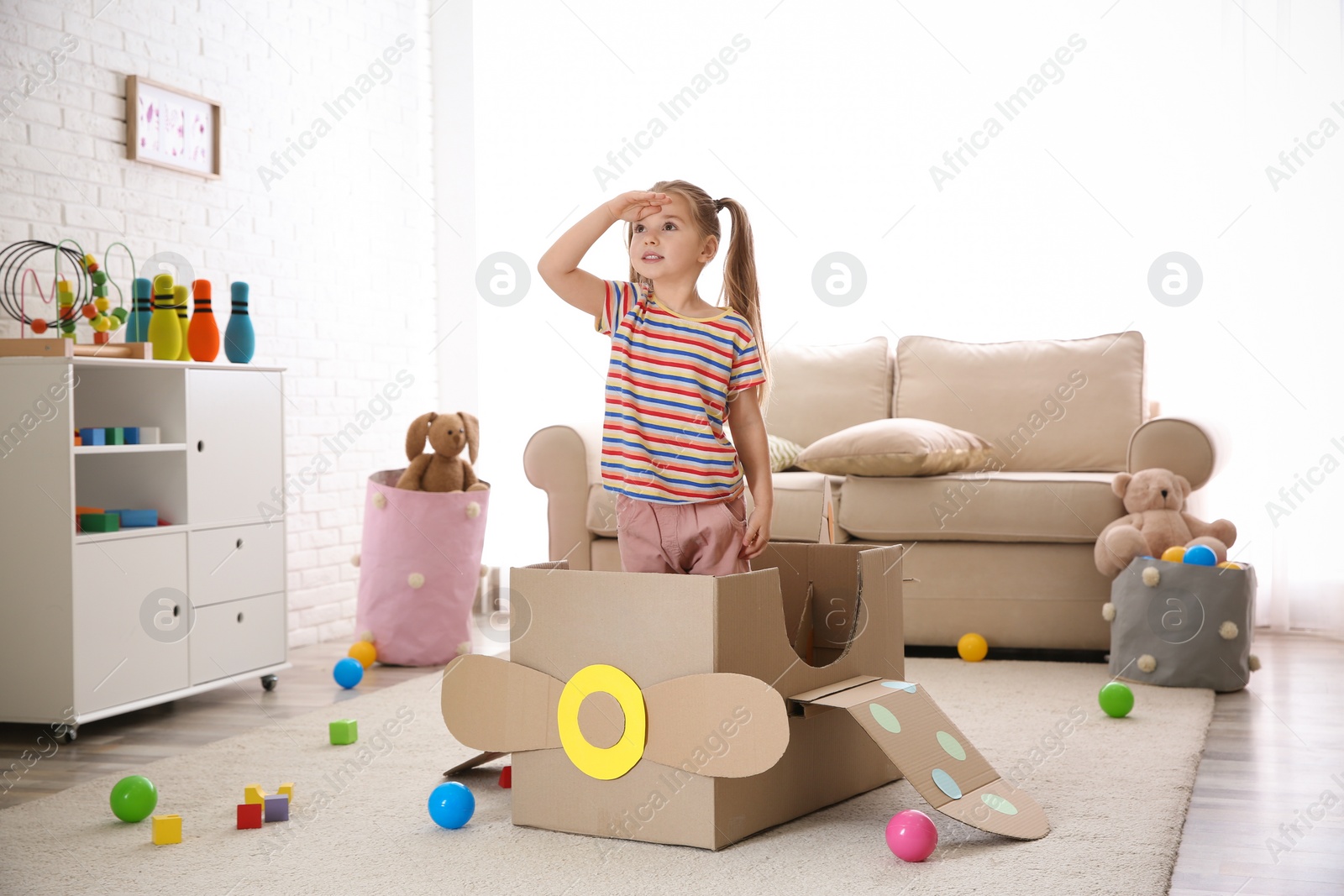 Photo of Cute little child playing with cardboard plane at home