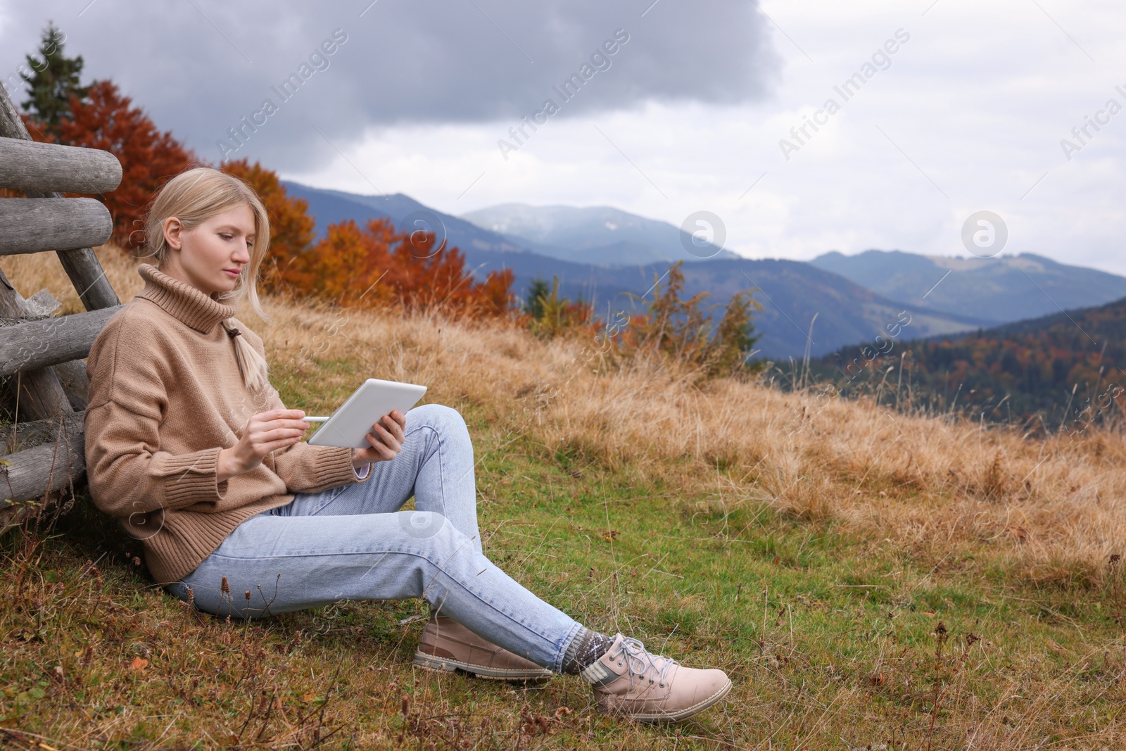 Photo of Young woman drawing on tablet in mountains, space for text