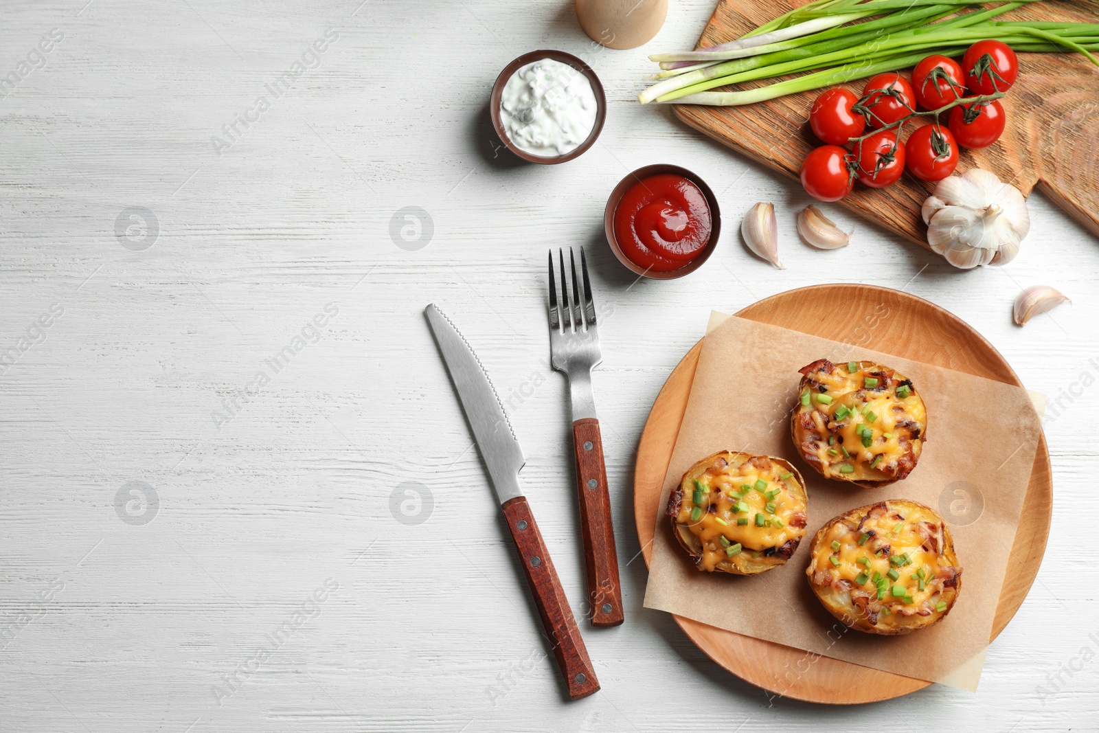 Photo of Flat lay composition with plate of baked potatoes, cutlery and space for text on wooden background