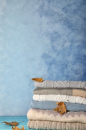 Photo of Stack of warm clothes with autumn leaves on table. Space for text