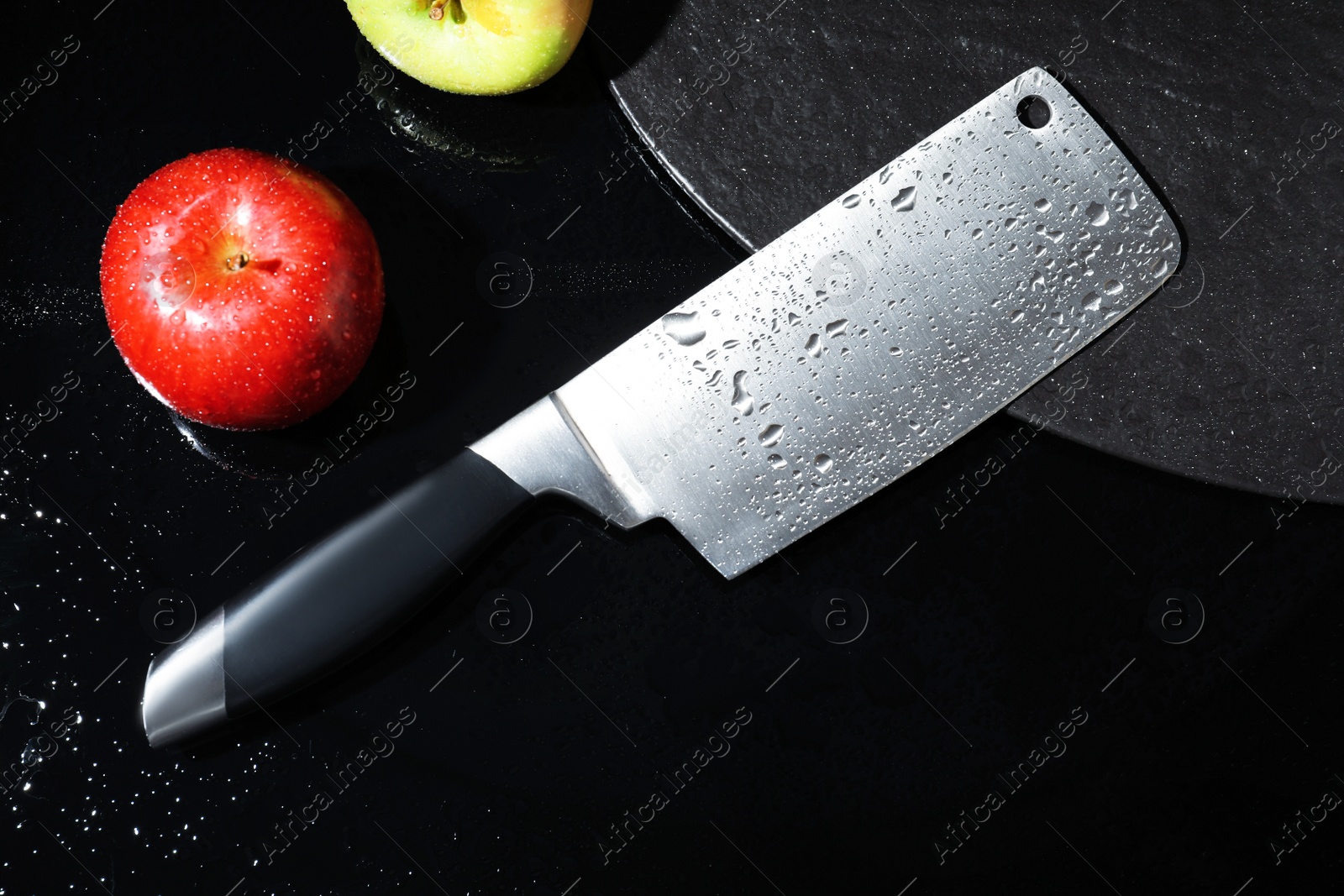 Photo of Cleaver and apples on wet black surface, flat lay
