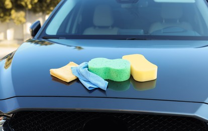 Photo of Sponges and rags on car hood outdoors. Cleaning products