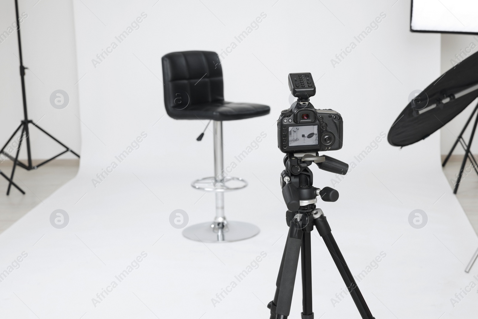 Photo of Camera on tripod, bar stool and professional lighting equipment in modern photo studio