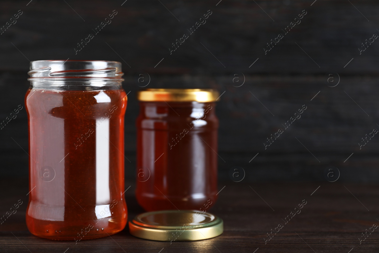 Photo of Jars of organic honey on wooden table against dark background. Space for text