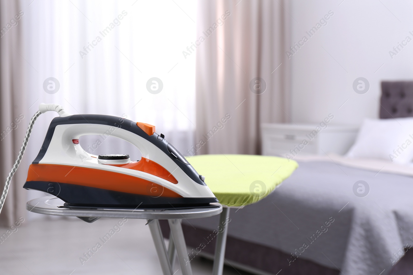 Photo of Modern electric iron on board in bedroom, space for text. Laundry day