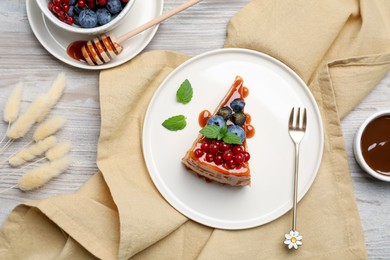 Photo of Slice of delicious cheesecake served with berries and caramel sauce on white wooden table, flat lay