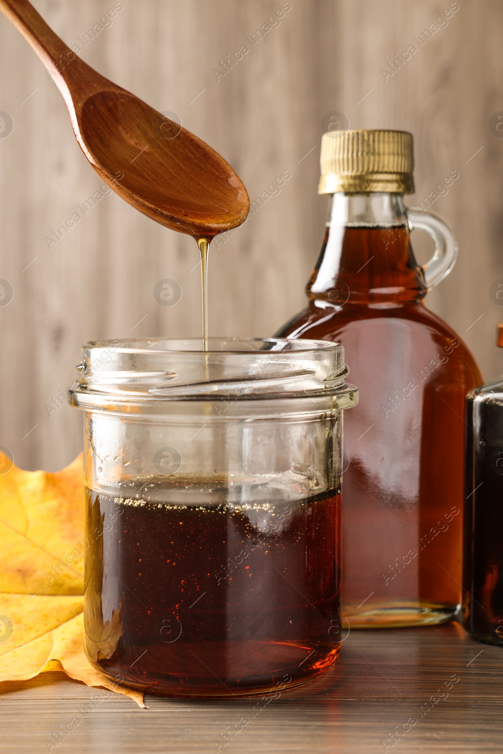 Photo of Spoon with tasty maple syrup over jar at wooden table