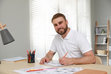 Young man coloring antistress picture at table indoors