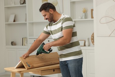 Photo of Man with electric screwdriver assembling furniture at table in room