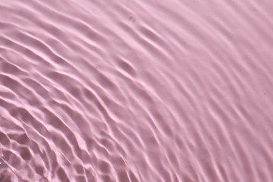 Rippled surface of clear water on pink background, top view