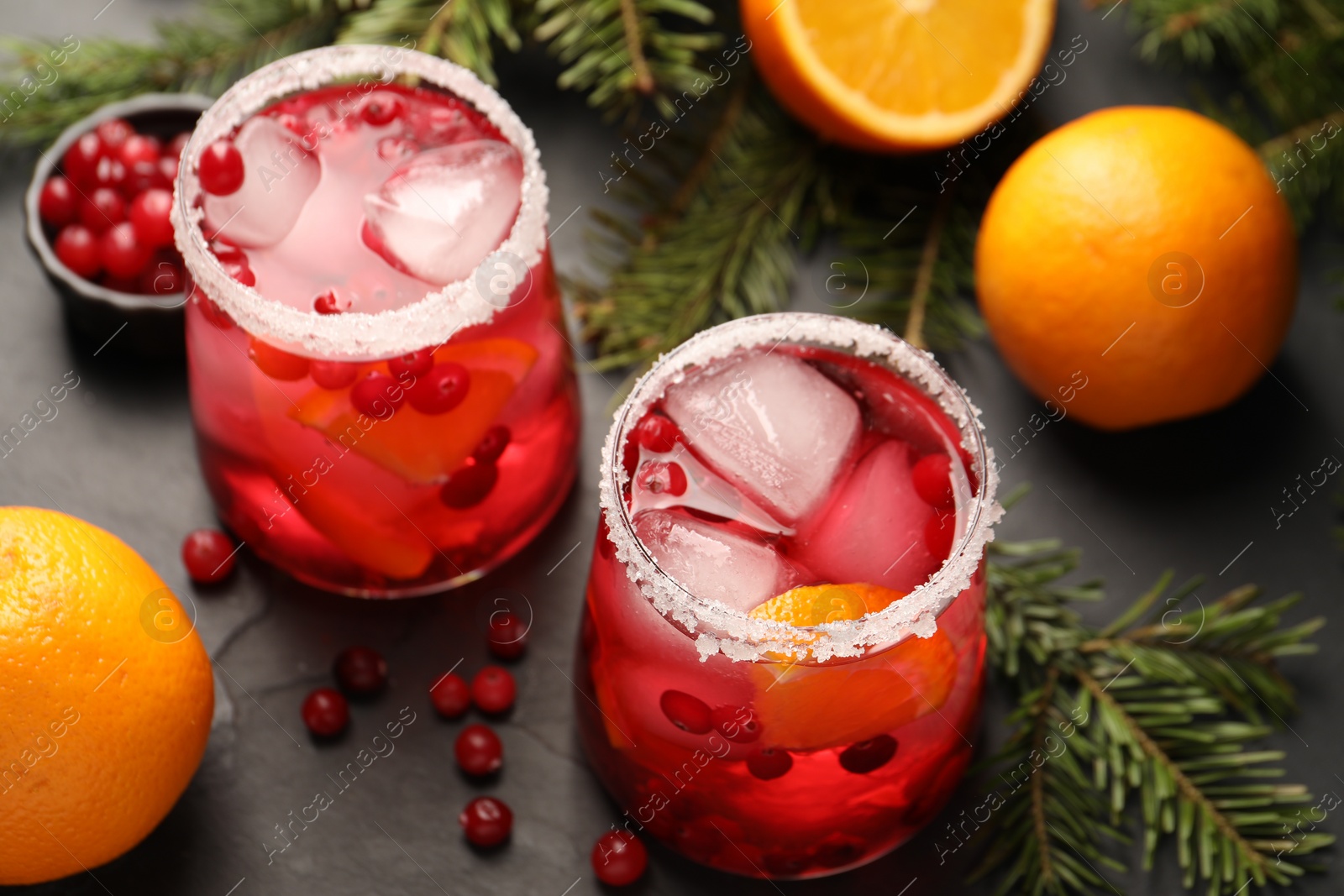 Photo of Tasty cranberry cocktail with ice cubes in glasses on dark gray table, closeup