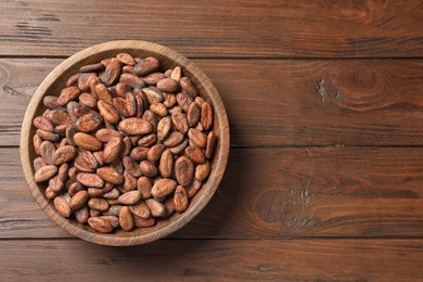 Photo of Bowl with cocoa beans on wooden table, top view. Space for text