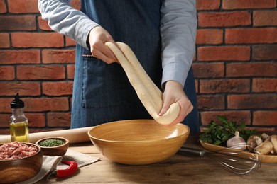 Photo of Woman kneading raw dough at wooden table, closeup