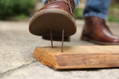 Photo of Careless man stepping on nails in wooden plank outdoors, closeup