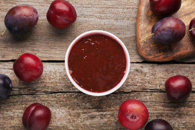 Plum puree in bowl and fresh fruits on wooden table, flat lay