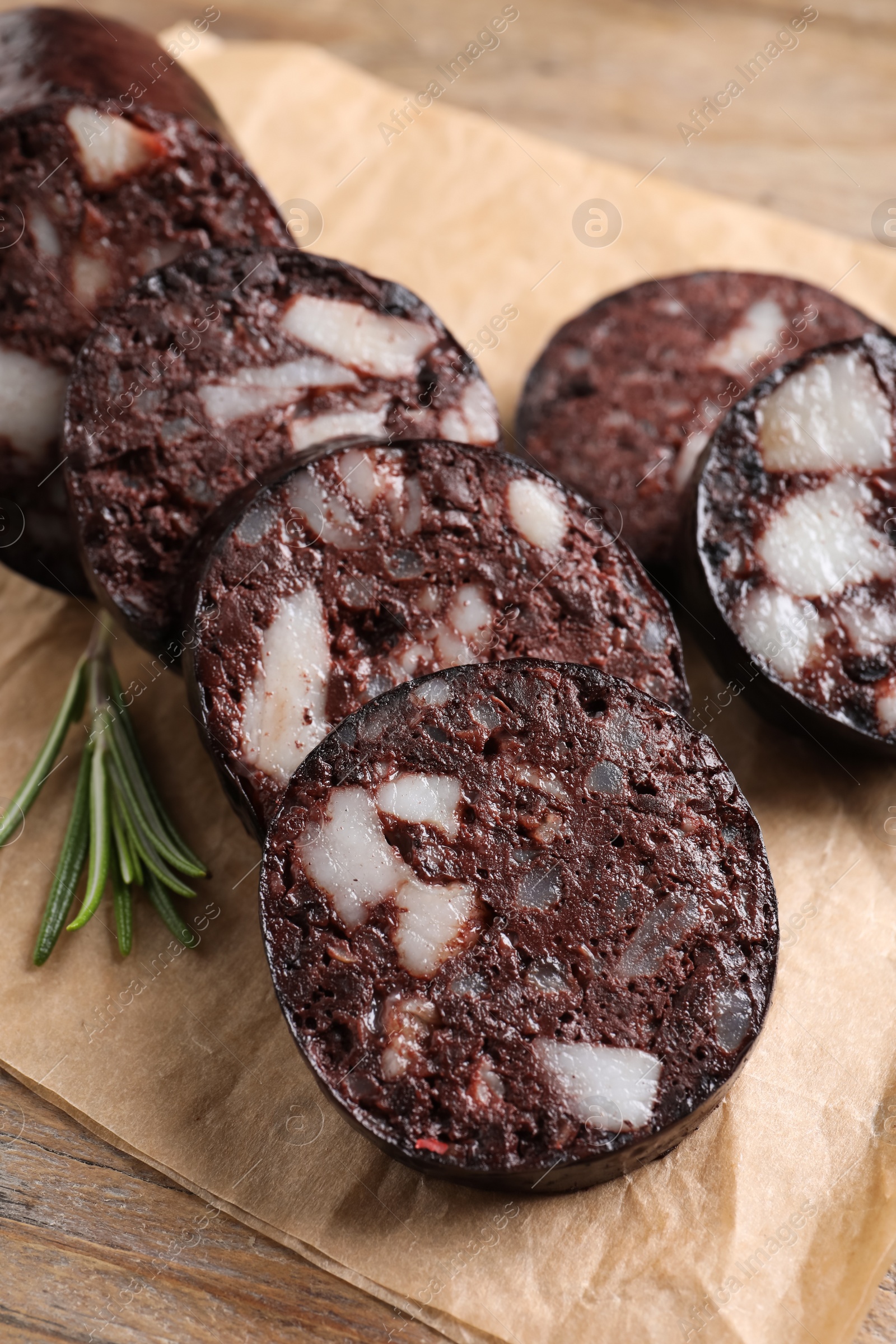 Photo of Slices of tasty blood sausage with rosemary on wooden table, closeup