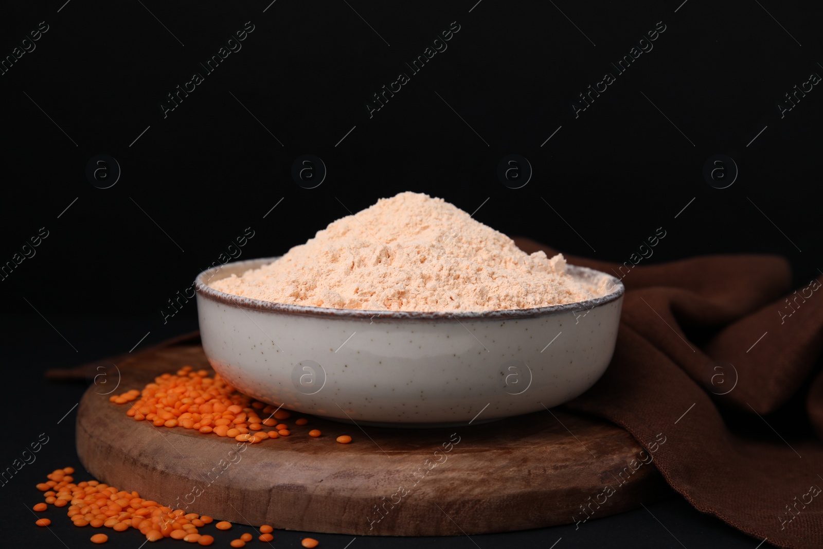 Photo of Bowl of lentil flour and seeds on dark table against black background