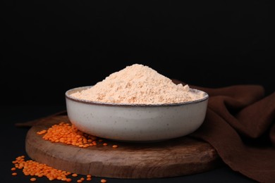 Photo of Bowl of lentil flour and seeds on dark table against black background