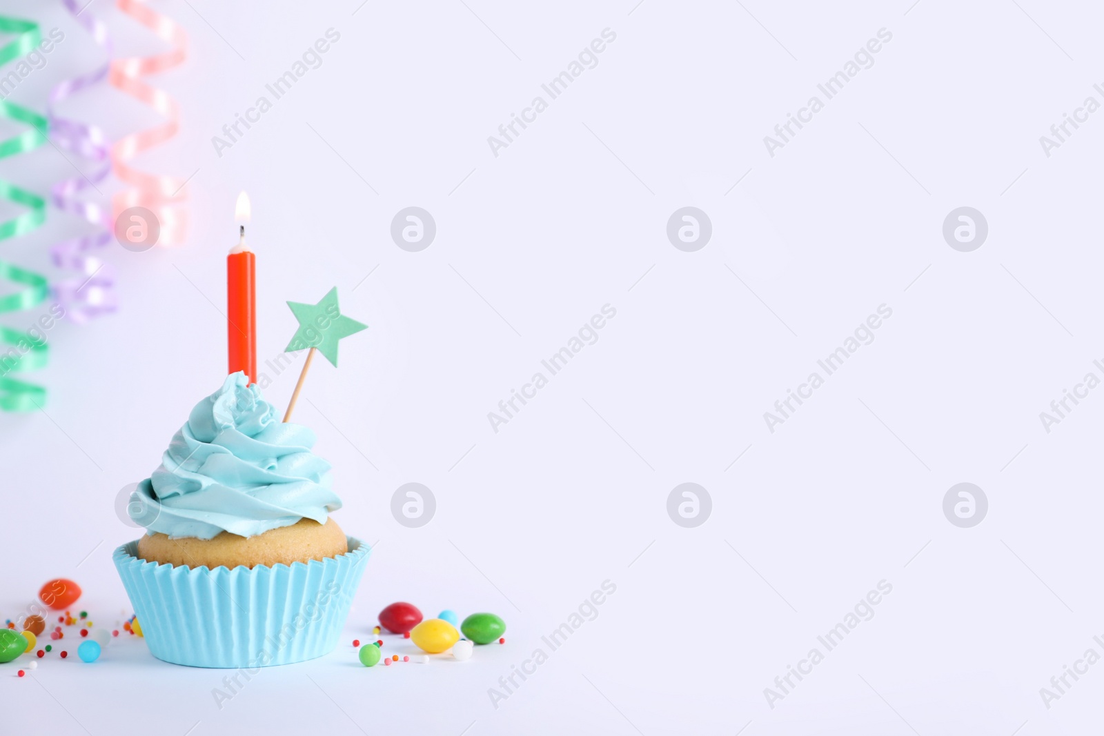 Photo of Delicious birthday cupcake with burning candle and candies on light grey background, space for text