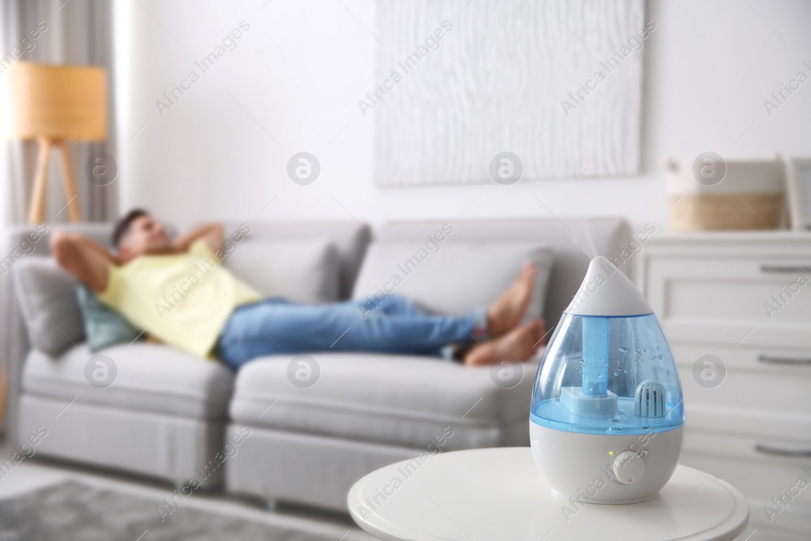 Photo of Modern air humidifier and blurred man resting on background