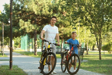 Photo of Dad and son riding bicycles in park on sunny day