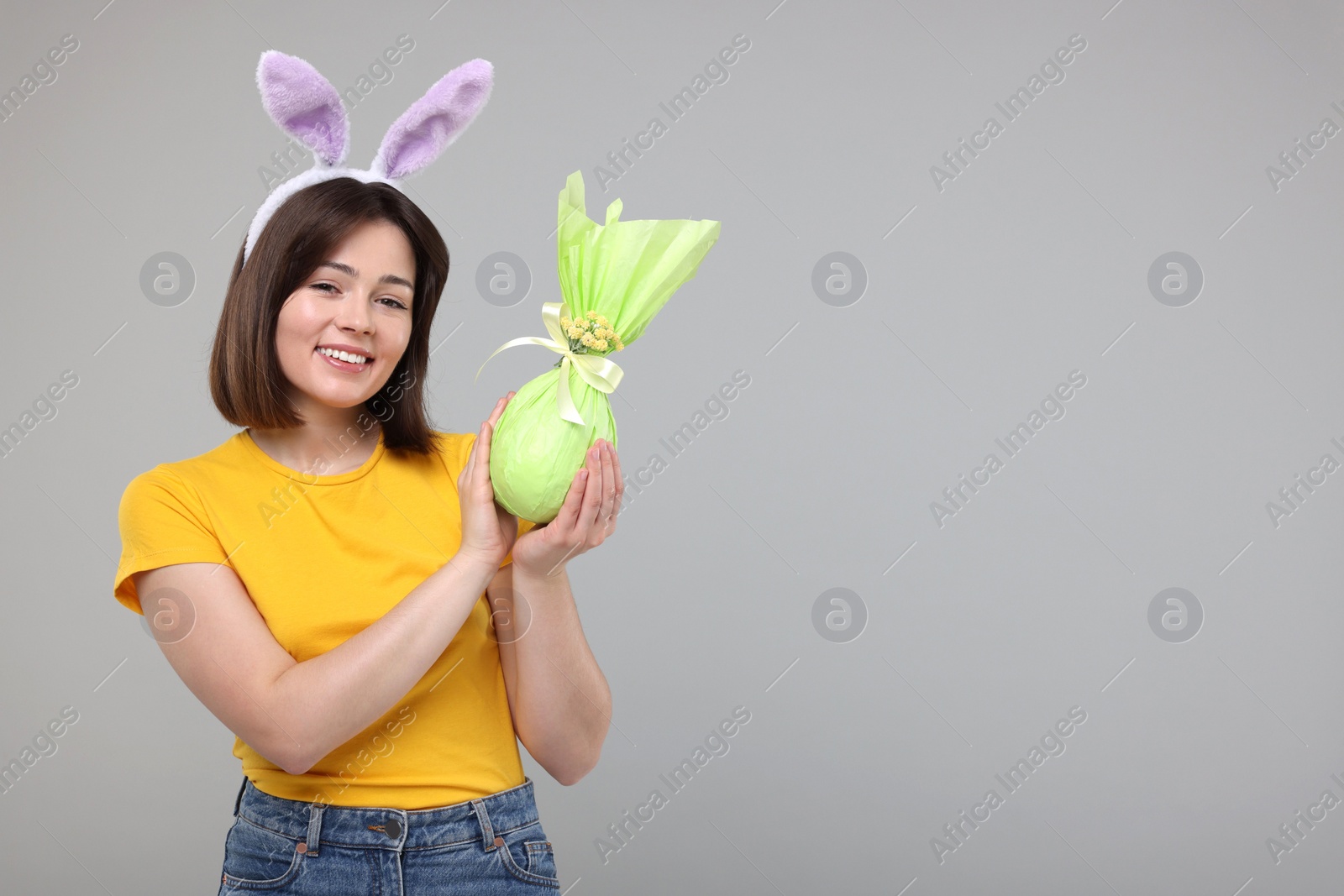 Photo of Easter celebration. Happy woman with bunny ears and wrapped egg on grey background, space for text