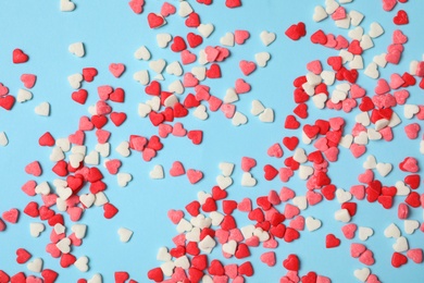 Photo of Bright heart shaped sprinkles on light blue background, flat lay