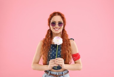 Stylish young hippie woman with dahlia flower on pink background