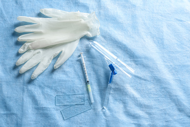 Photo of Anoscope, rubber gloves and syringe on light blue fabric, flat lay. Hemorrhoid treatment